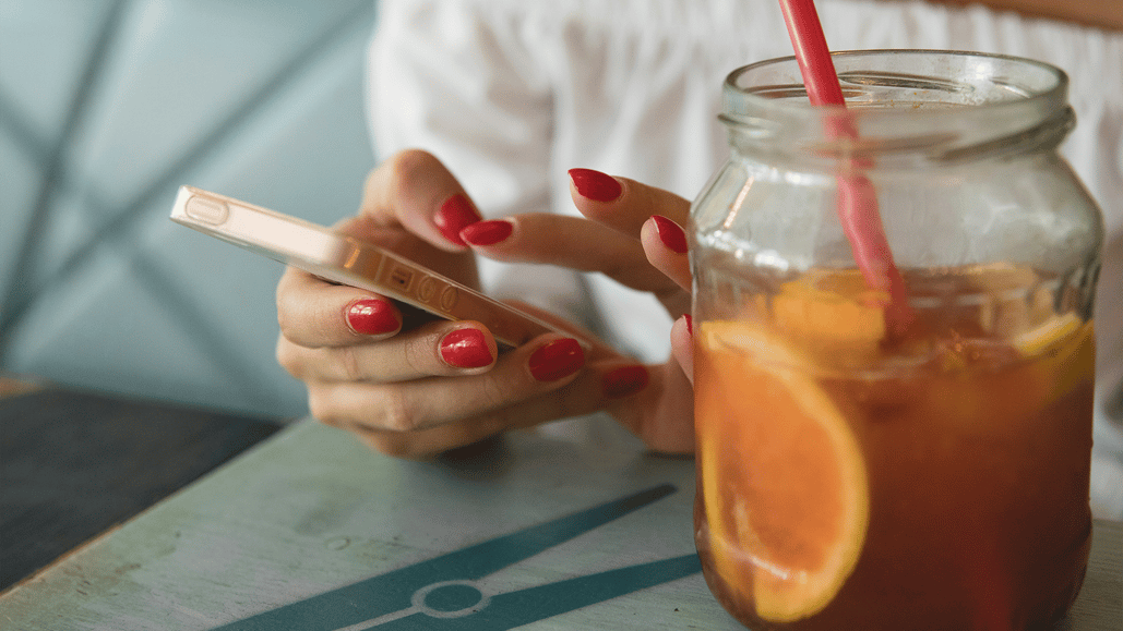 A woman drinks iced tea, while using Adobe Premiere for iPhone to edit a video
