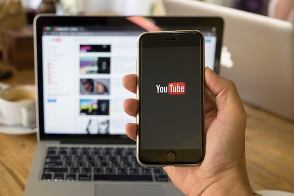 Phone-featuring-YouTube-logo-in-front-of-laptop-with-YouTube-website
