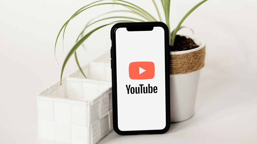 A smart phone props up on a plant, while loading songs for youtube shorts