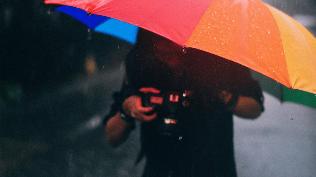 A man holding a camera under an umbrella, making a video while also recording storm sound effects.
