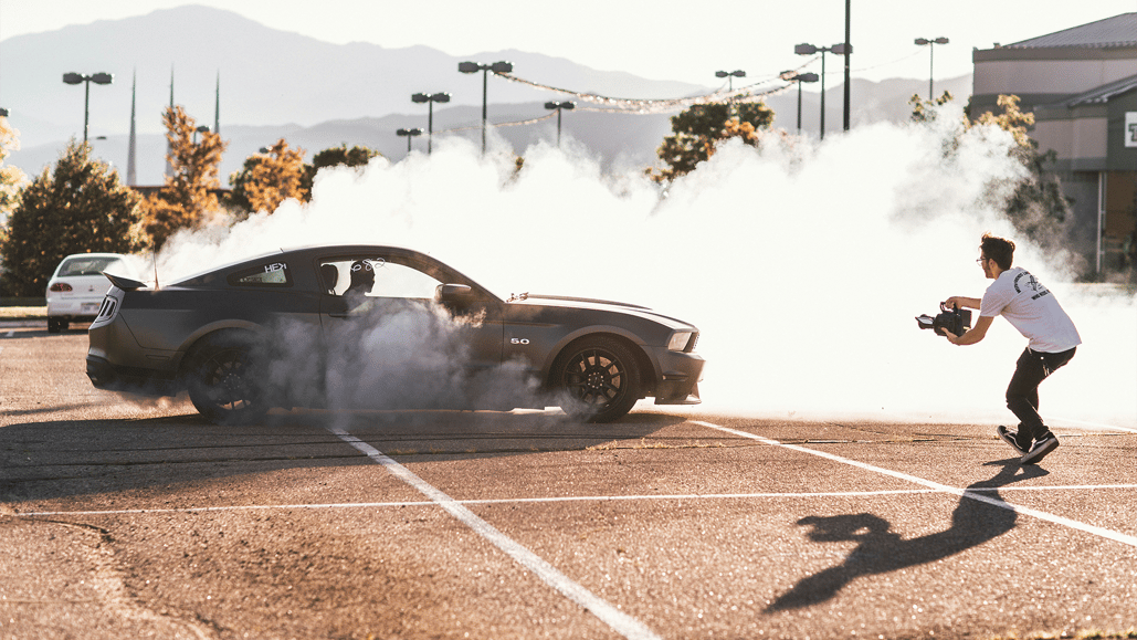 A person records a car in a cloud of smoke for a series of YouTube challenge videos