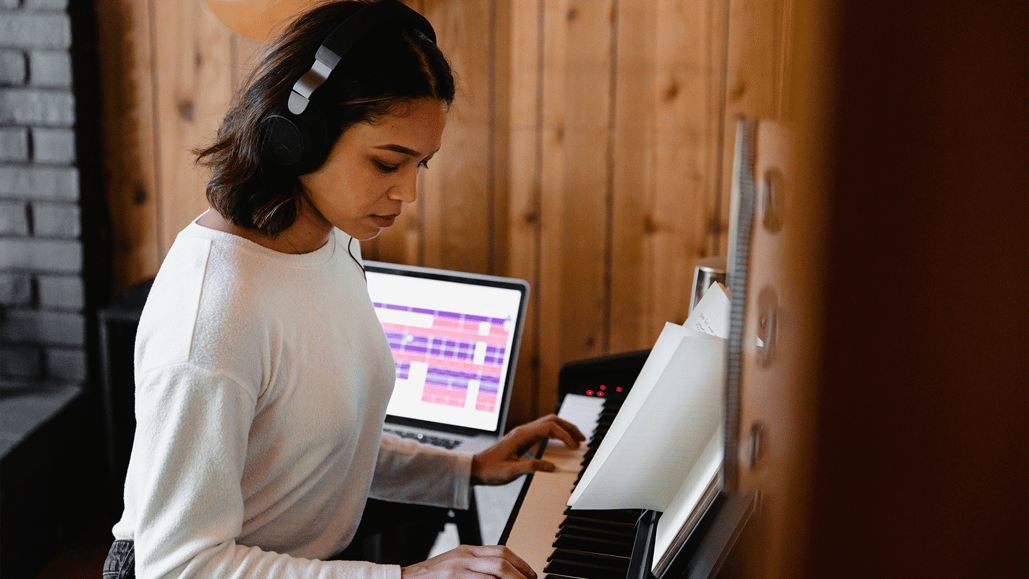 A woman in a recording studio is playing the piano and exploring the ethical use of AI generated songs for her video projects.
