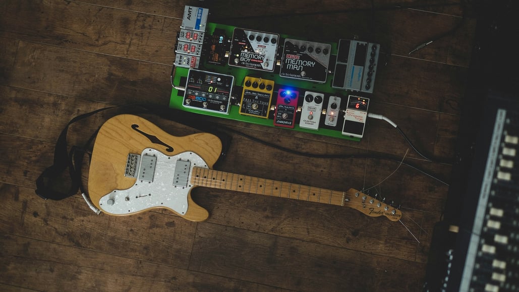 Fender guitar on a hardwood floor with pedals nearby