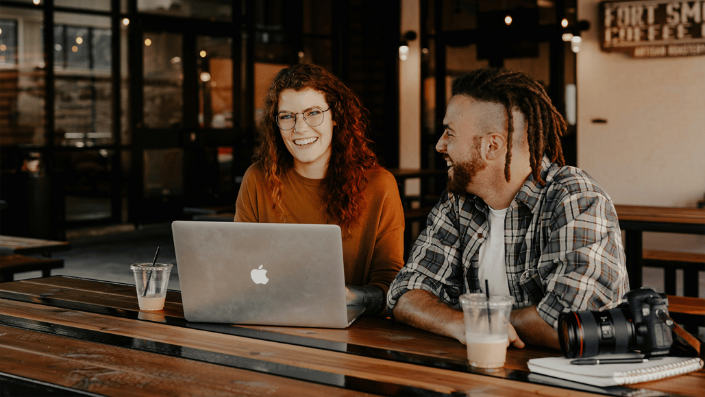 A man and a woman sit at a table in a coffee shop discussing music licensing options, including song licensing costs and music licensing subscription costs.