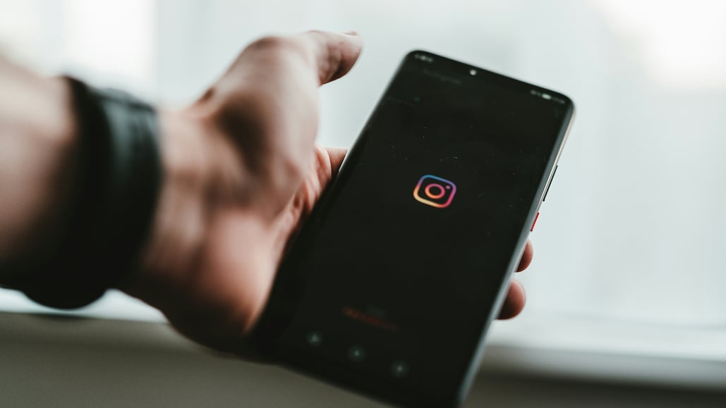 A person holds a smartphone loading the instagram app, as they wonder about how to use copyrighted music on Instagram reels.