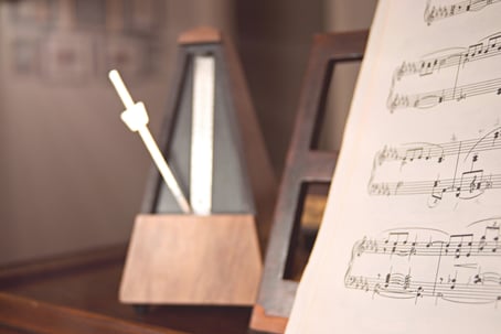 A metronome stands behind a book of sheet music, ready to set the pace for mid tempo music to be played