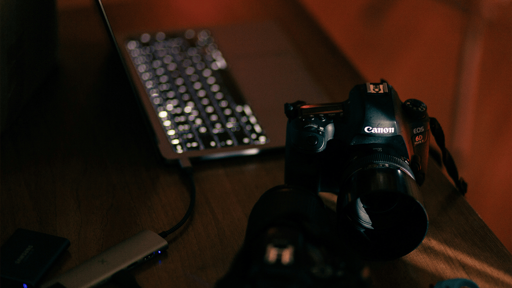 A camera sits beside a laptop computer, while the creator tries to download music for iMovie.