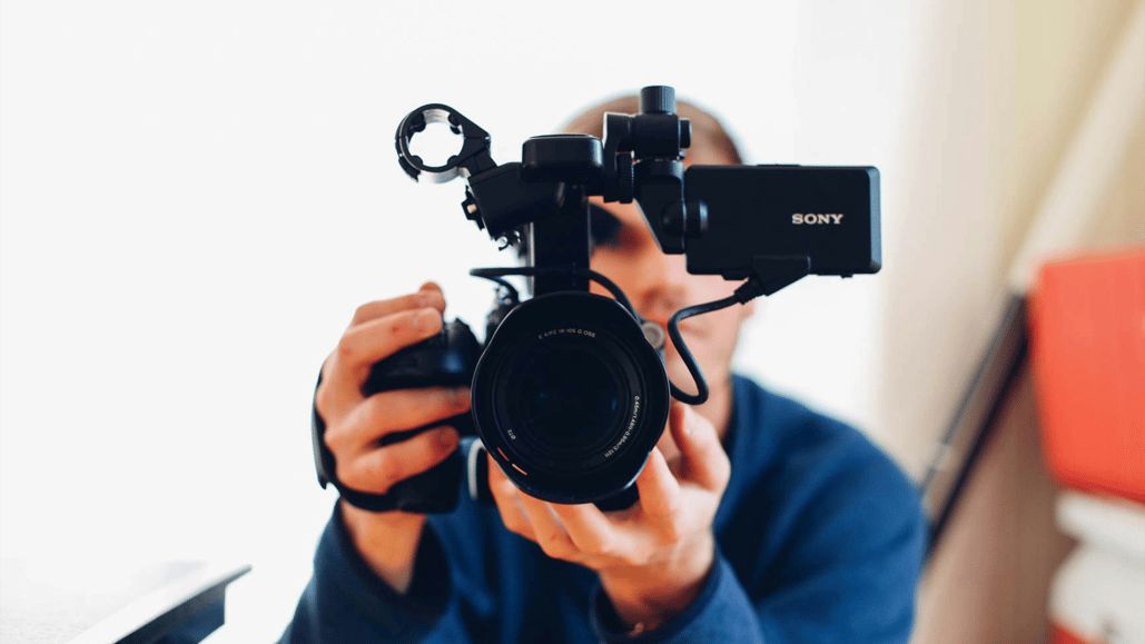 A man holds up a video camera, recording content for one of his most profitable YouTube channel ideas.