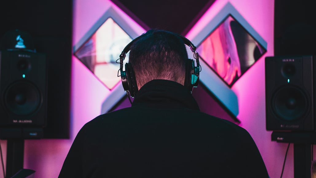 A man wears headphones and sits between 2 speakers, listening to 8d surround sound.